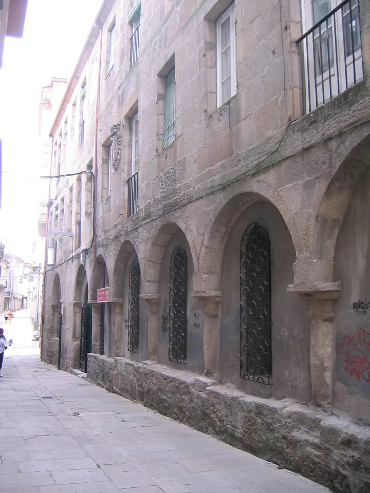 Calle estrecha de piedra junto a un viejo edificio de granito con ventanas en arco en la planta baja y balcones de hierro