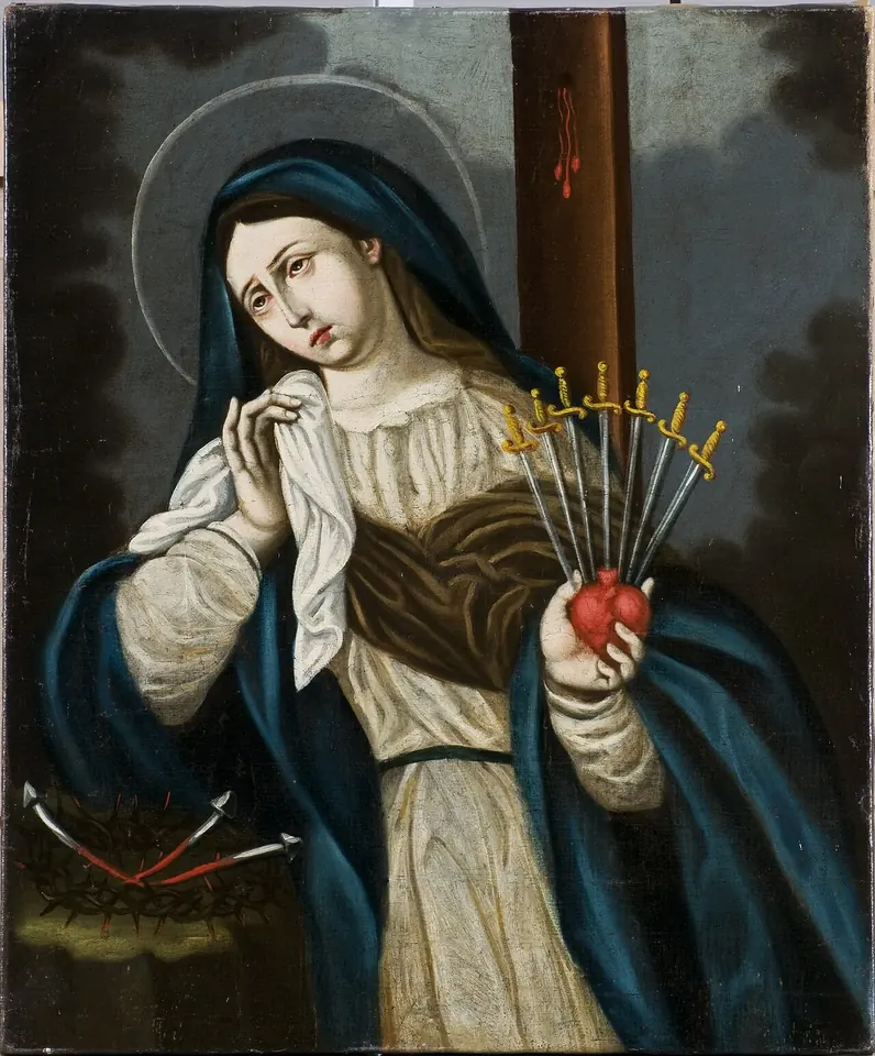 La Virgen María con manto azul que llora con un paño blanco ante la cruz y sostiene un corazón rojo atravesado por siete pequeñas espadas