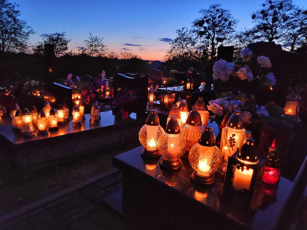 Faroles de vidrio rojos, blancos y ámbar encendidos sobre tumbas con flores al anochecer