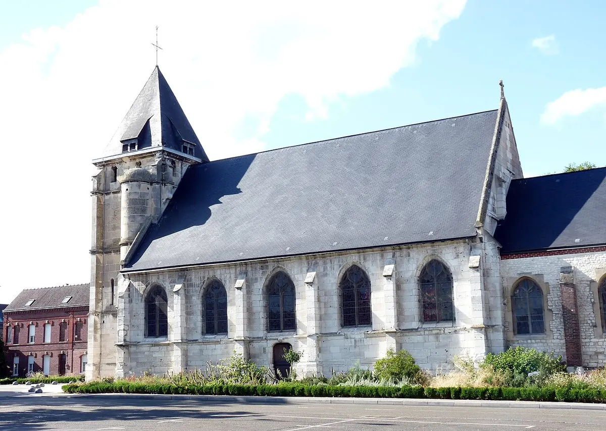 Gray stone church with a square bell tower and slate spire and a long slate roof, beside a small paved square and red-brick houses