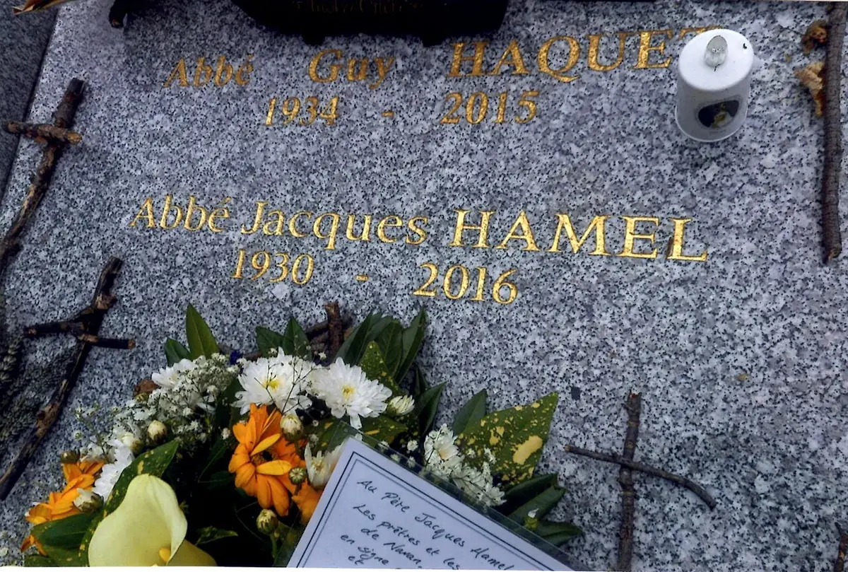 Gray granite grave slab with gold lettering reading Abbé Jacques Hamel 1930 to 2016, covered with fresh flowers