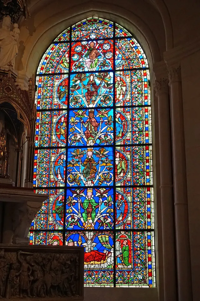 Arched stained-glass window glowing in blue, red and green, showing a vine rising from a reclining figure at the bottom through kings to the Virgin and Christ, with prophets in the side panels