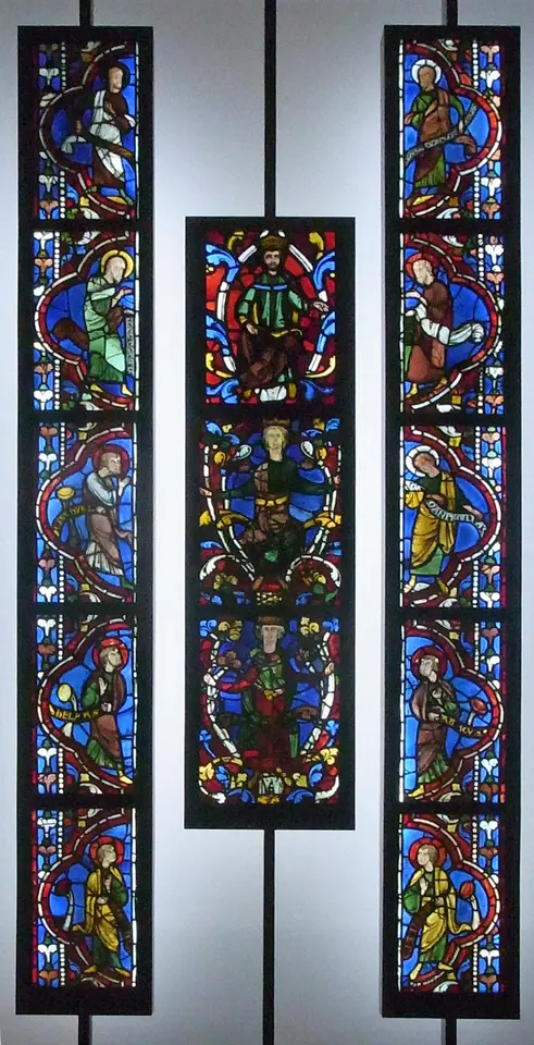 Three tall strips of medieval stained glass displayed in a museum, the middle one showing crowned kings seated on the branches of a vine, the outer ones showing standing prophets