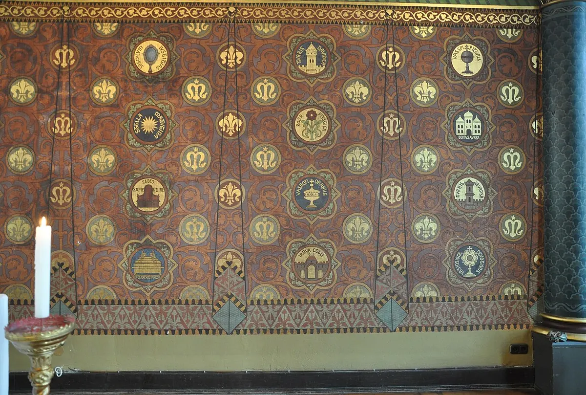 A wall painted like a brown and gold canopy, covered with rows of small round medallions showing a tower, a house, an ark, a star, a rose and other symbols