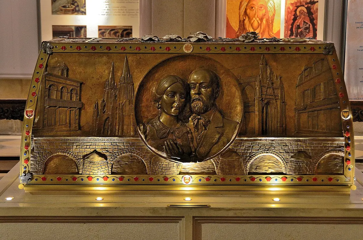 A gilded bronze reliquary chest with a round medallion of the couple's faces at the center and reliefs of the churches of Alençon and Lisieux on either side