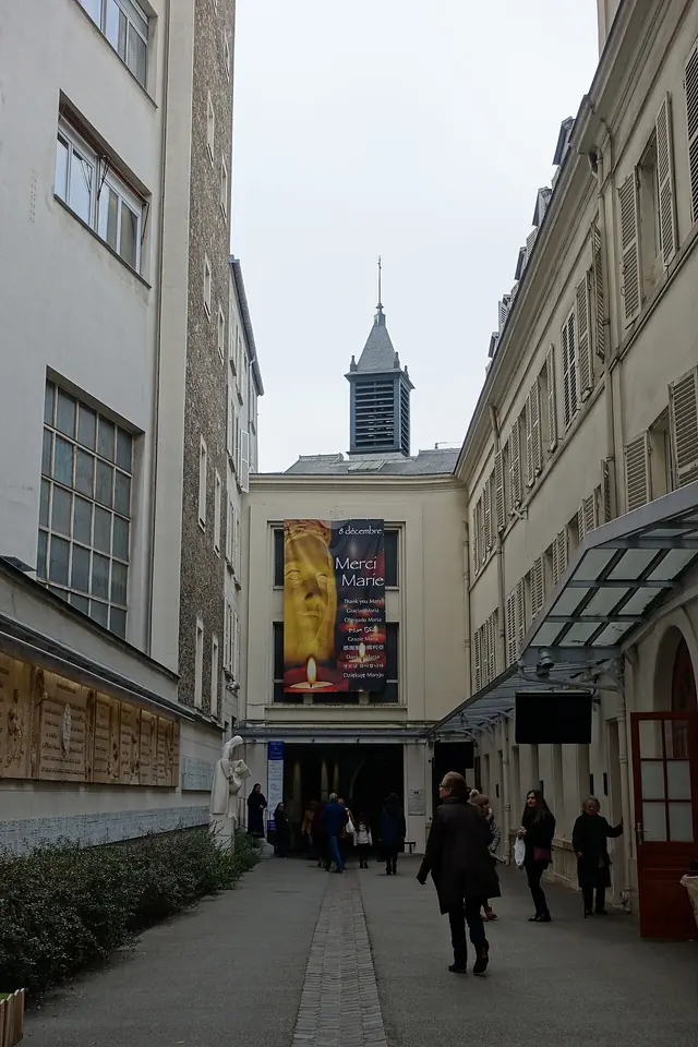 Pilgrims walking down the narrow passage from the rue du Bac toward the entrance of the Chapel of Our Lady of the Miraculous Medal in Paris