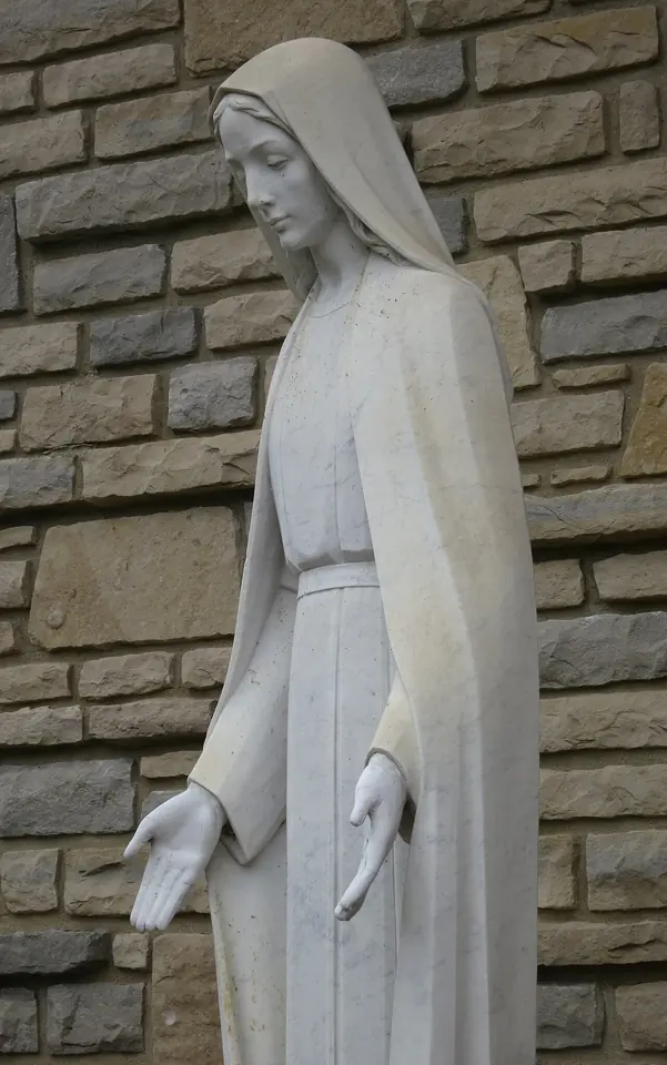 White stone statue of the Virgin Mary with her hands lowered and open, against a stone wall at an Ohio parish dedicated to Our Lady of the Miraculous Medal