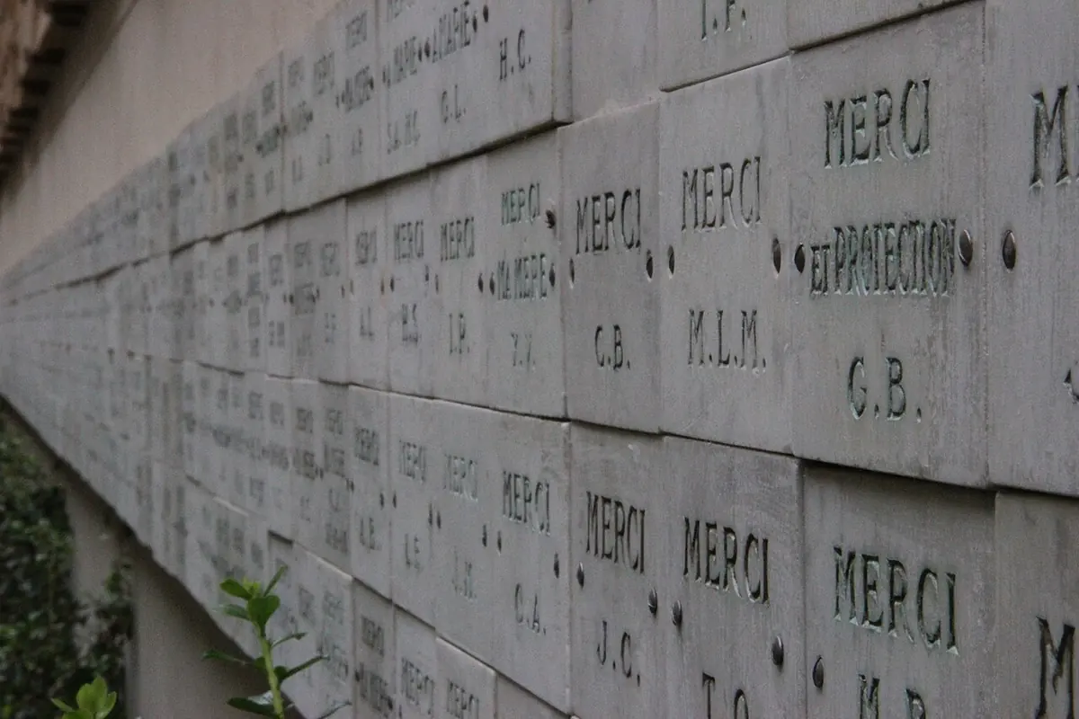 A stone wall covered with ex-voto plaques carved with the word Merci and initials, in the courtyard of the Chapel of the Miraculous Medal in Paris