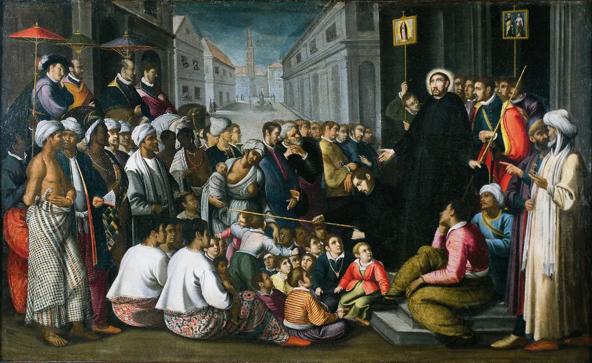 A Jesuit priest in a black cassock preaches from a step to a large crowd of men, women and children in colorful clothes and turbans in a city square