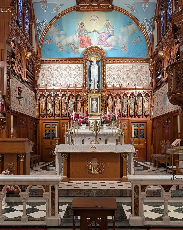 A marble altar before carved wooden panels with statues of the apostles, the Divine Mercy image at the center, a white statue of Mary above it, and a painted dome of the Trinity crowning Mary