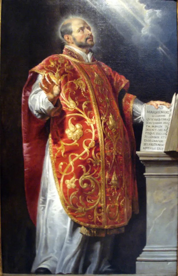 Un sacerdote calvo y barbado, con casulla roja y dorada ricamente bordada, levanta los ojos al cielo con la mano sobre un libro abierto