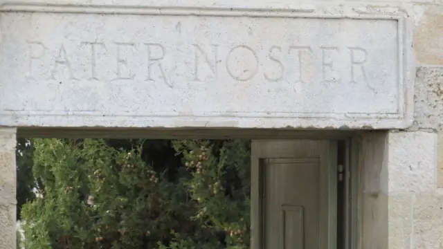 Dintel de piedra tallado con las palabras PATER NOSTER sobre una puerta, con la vegetación de un jardín al fondo
