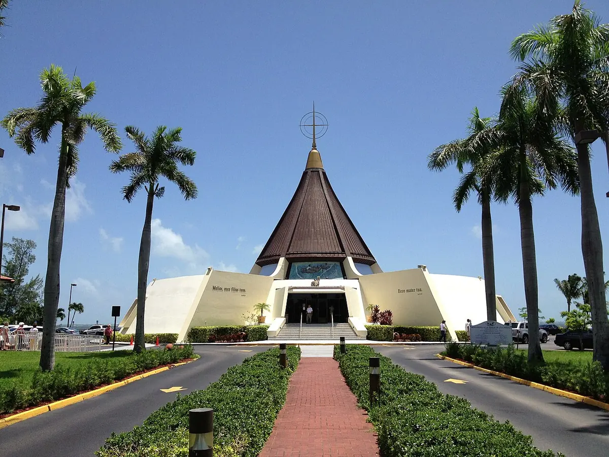 The cone-shaped modern shrine of Our Lady of Charity in Miami, its brown roof rising to a cross, at the end of a brick path lined with palm trees