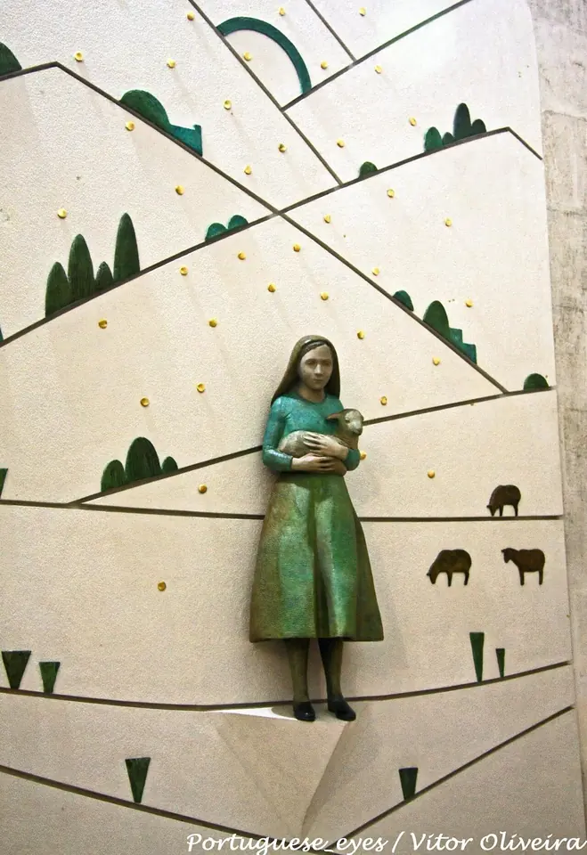 A side chapel of the basilica with a stone tomb in the floor and a statue of a small girl above it, with flowers