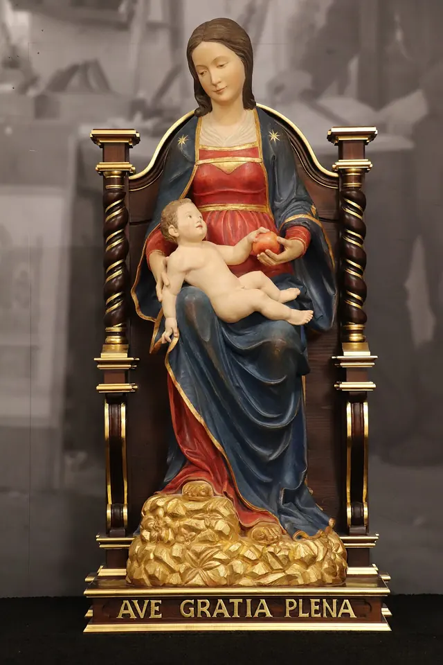Painted wooden statue of the Virgin seated on a carved throne in a red dress and blue mantle, holding the Christ Child, on a base inscribed "Ave gratia plena"