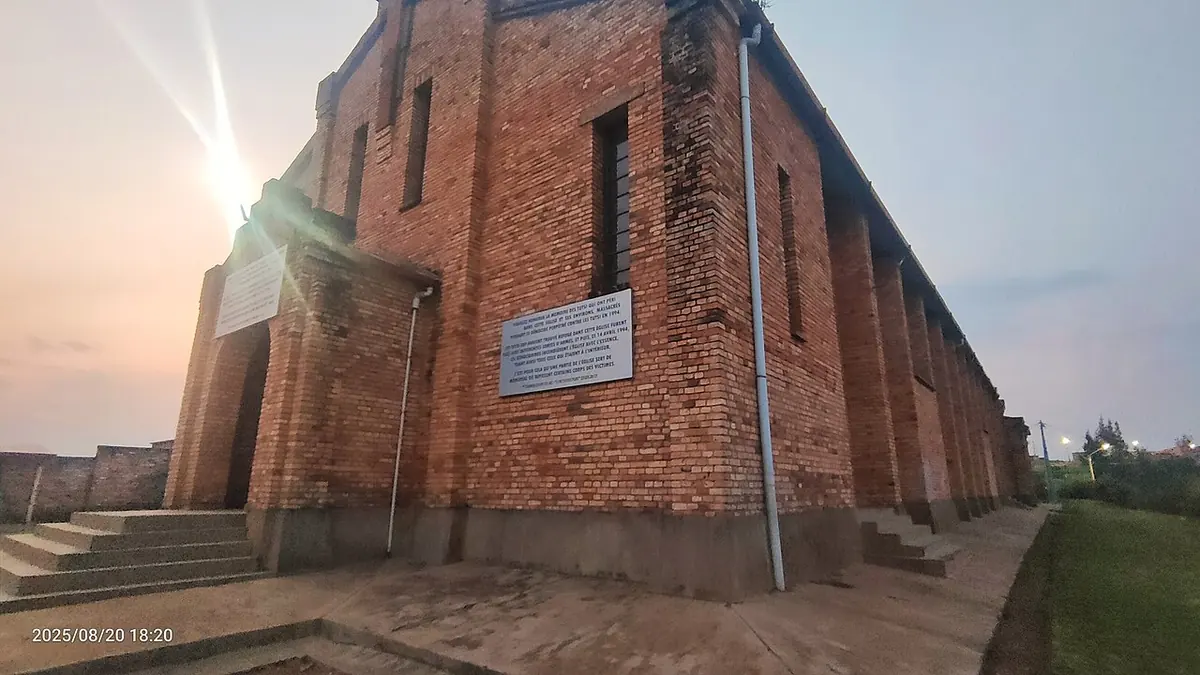 The tall brick side wall of a church at dusk, with steps leading to a doorway and a white memorial plaque fixed to the wall