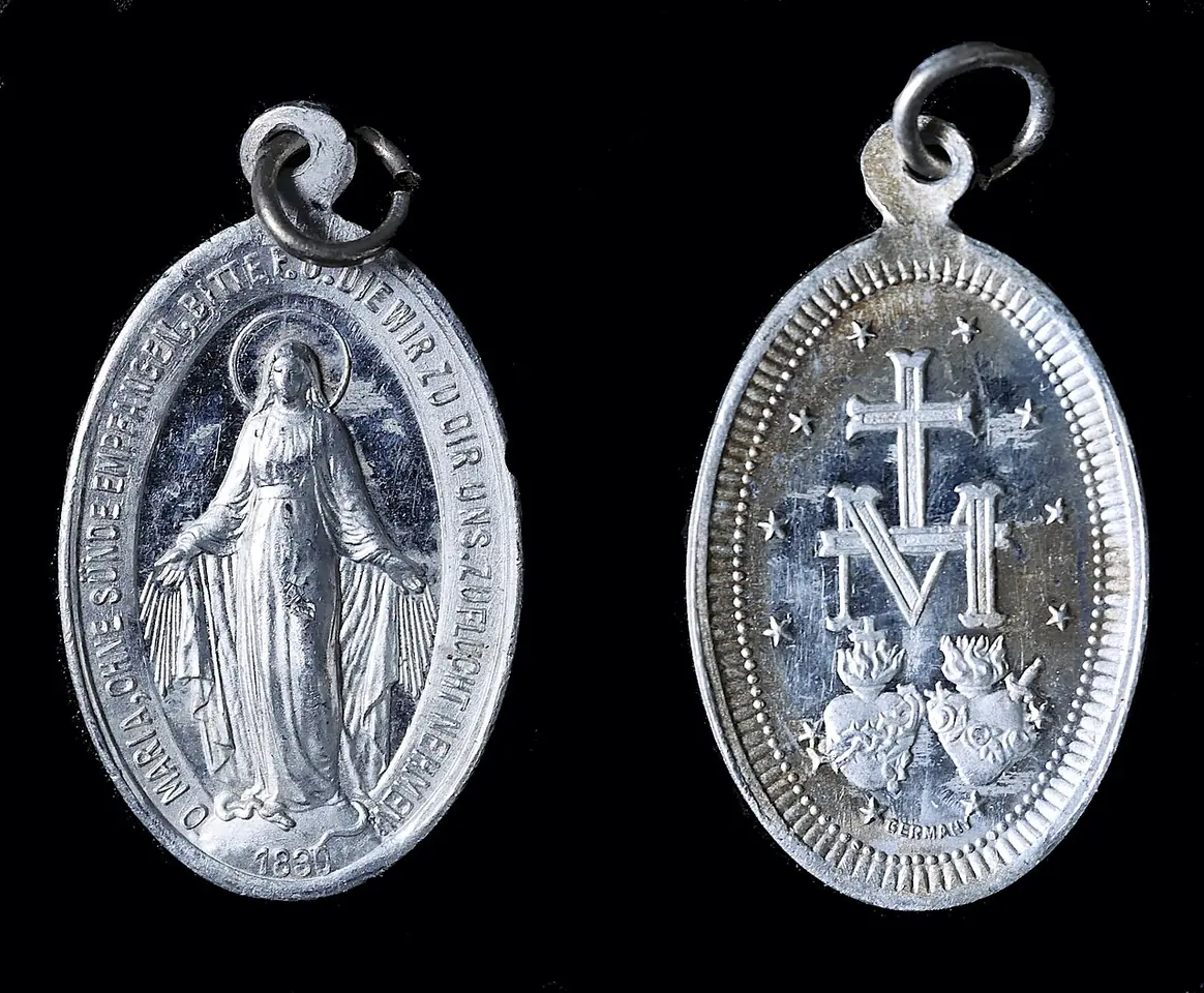 Front and back of a small silver-colored oval medal with a ring for a chain, showing the Virgin with rays on one side and the M, cross, hearts and stars on the other