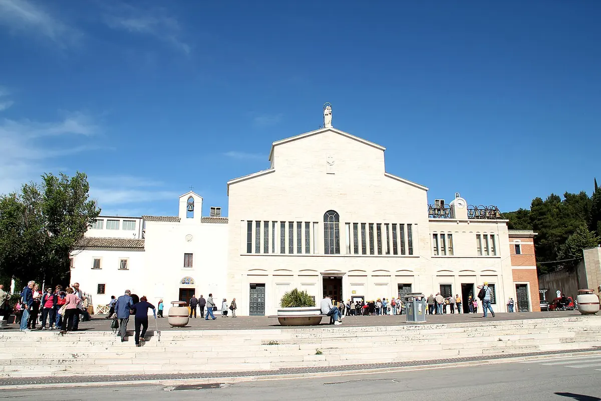The simple white facade of the old friary church beside the larger modern church of Santa Maria delle Grazie, with pilgrims on the square in front