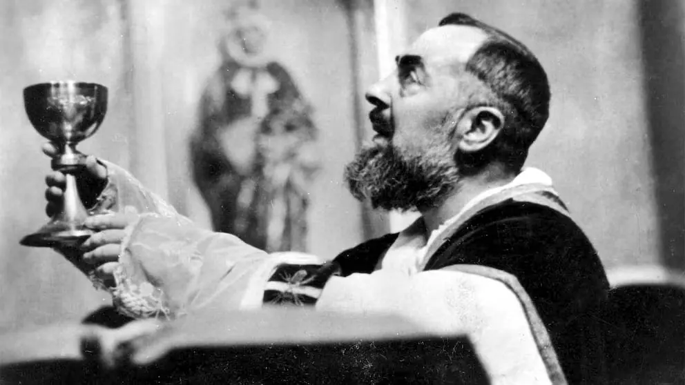 Black-and-white photograph of Padre Pio in vestments at the altar, raising the chalice and looking up
