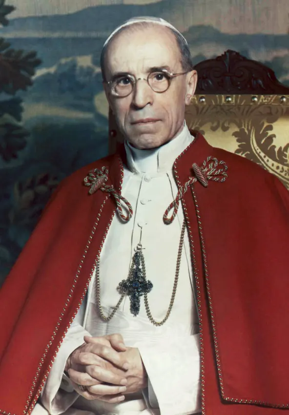 Color portrait of a thin, elderly pope in round glasses, white skullcap and red cape trimmed with ermine, his hands folded over a pectoral cross