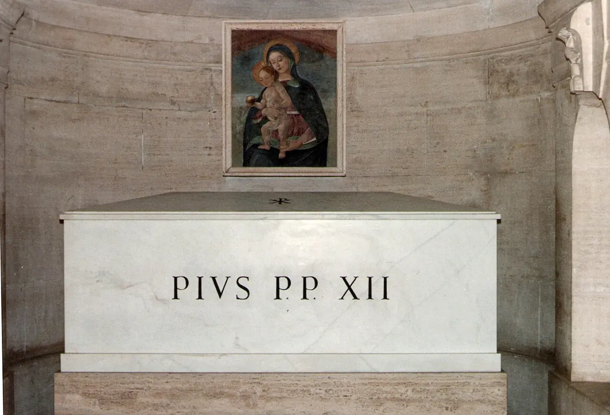 A plain white marble sarcophagus inscribed PIVS PP XII in an alcove, below a small painting of the Madonna and Child