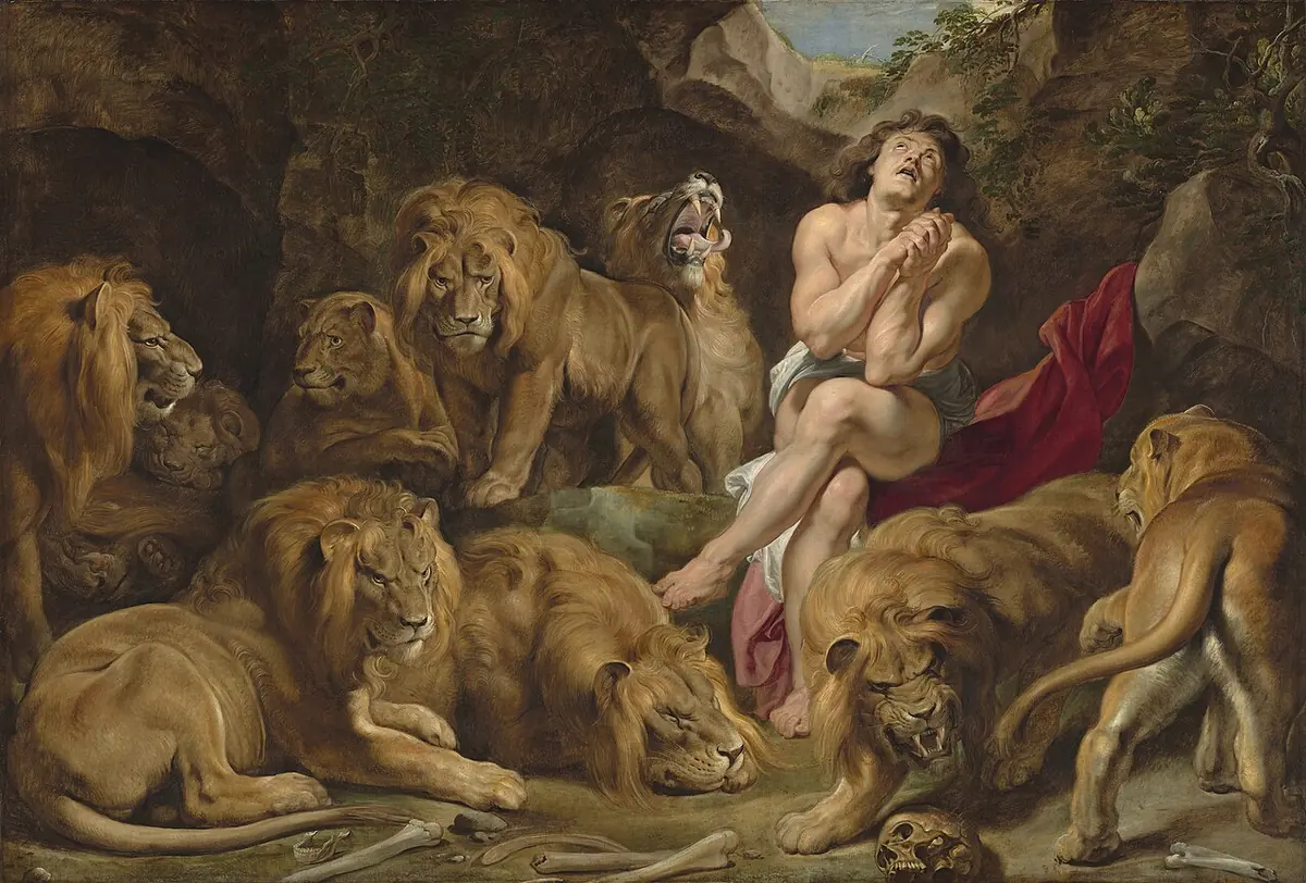 The prophet Daniel sits nearly naked on a rock in a dark den, hands clasped and eyes raised to heaven, surrounded by full-sized sleeping and prowling lions