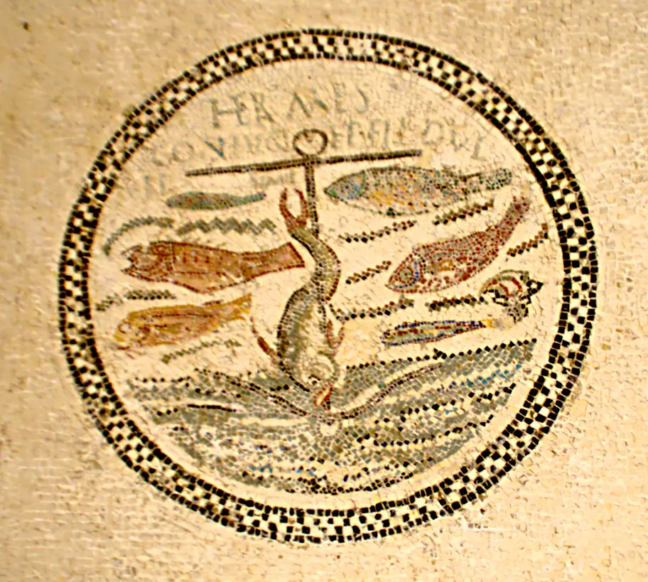 A round early Christian mosaic with an inscription above an anchor, a dolphin wrapped around its shaft and fish swimming on either side