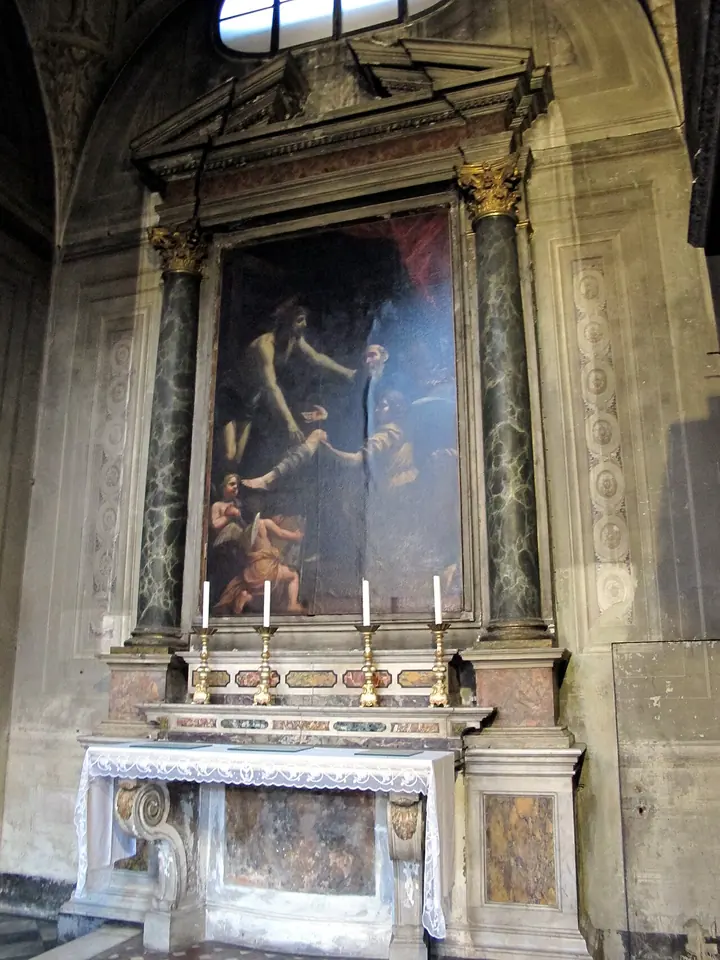 A marble side altar with dark columns framing a large painting of Christ reaching down from the cross to a kneeling friar
