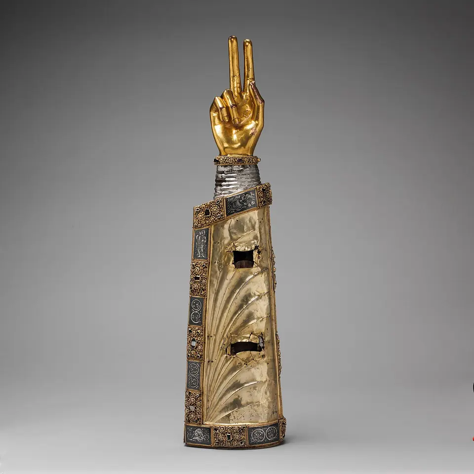 Silver reliquary shaped like a forearm in a pleated sleeve, with a gilded hand raised in blessing and small windows set with crystal