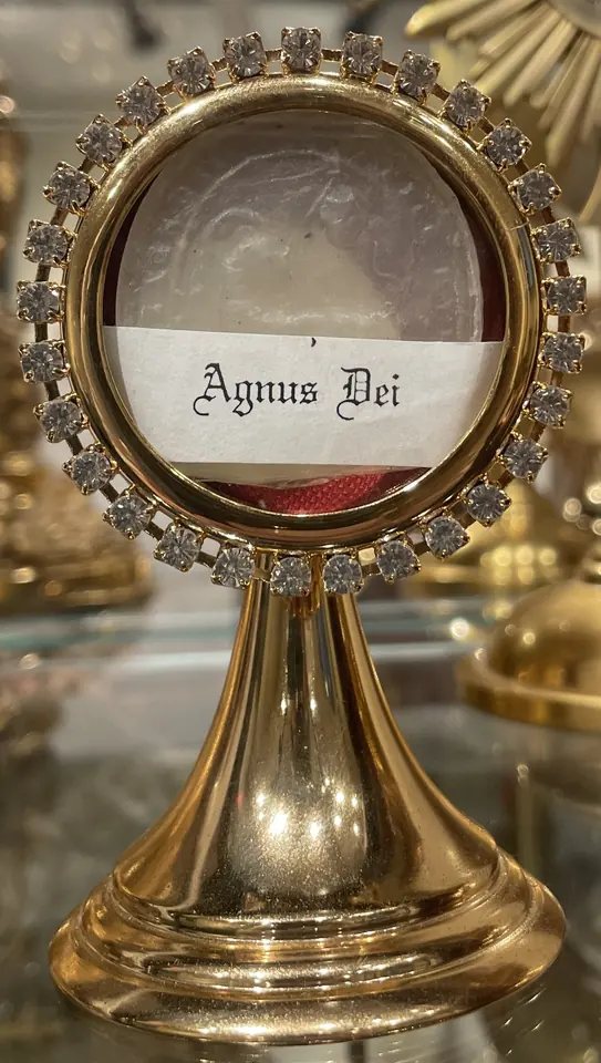A small round wax disc labeled Agnus Dei displayed in a gilt stand ringed with clear stones