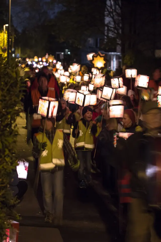 Children and parents walking down a dark street in Cologne carrying glowing paper lanterns in a St. Martin's Day procession