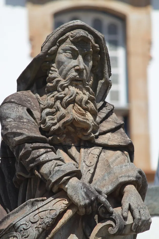 Soapstone statue of a bearded prophet in a hooded cloak, leaning on a carved scroll