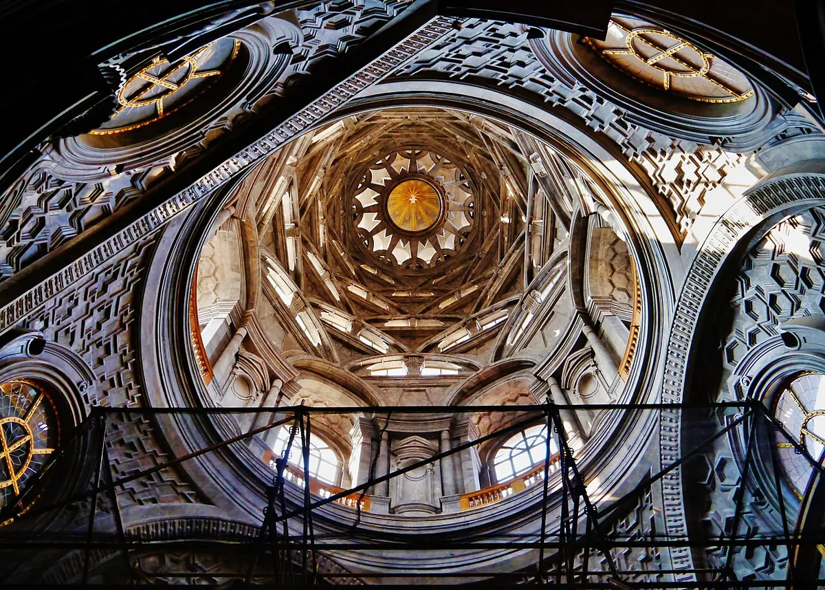 Looking up into a dark stone dome made of stacked, interlocking arches that rise toward a bright star-shaped opening, with round windows below