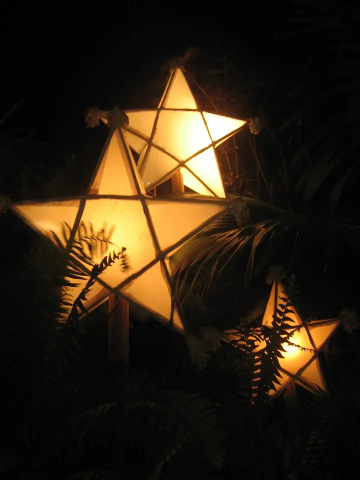 Three five-pointed star lanterns made of bamboo and paper glowing warm yellow at night among dark palm leaves