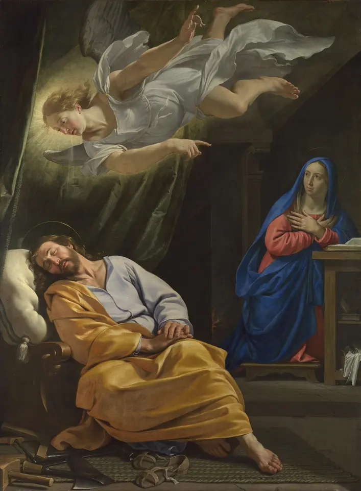 Painting of Joseph asleep in a chair with his head on his hand while an angel descends and points toward Mary, who kneels in prayer in the background