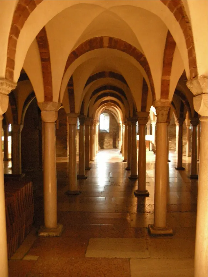 Low crypt with rows of slender stone columns and brick vaults lit with warm light, stretching back toward an altar