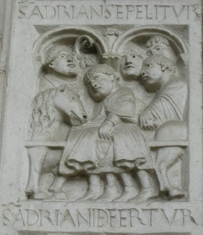 Romanesque stone relief of men carrying a body on a bier slung between horses, under arches, with a Latin inscription above