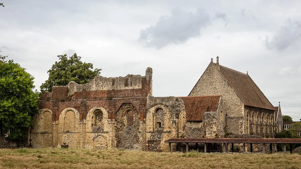 Wide view of the ruined walls of St. Augustine's Abbey in Canterbury with a later stone hall behind, under a cloudy sky