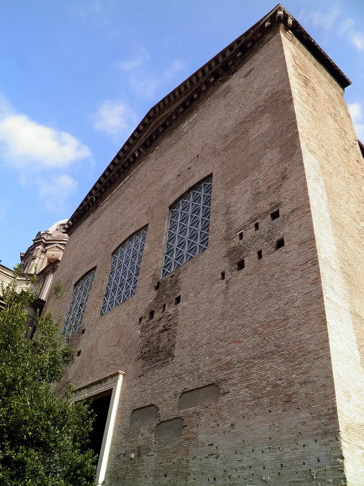 The tall, plain brick front of the ancient Roman Senate House in the Forum, with a bronze door at the top of a flight of steps