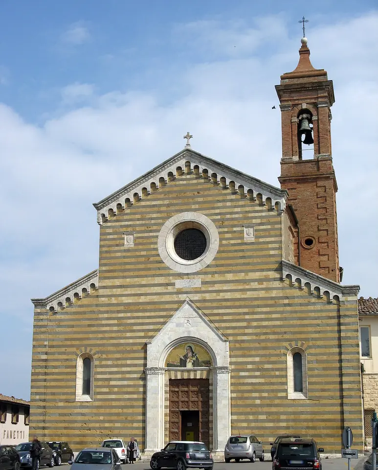 Striped stone facade of a church with a rose window and a mosaic over the door, beside a brick bell tower, on a square with parked cars