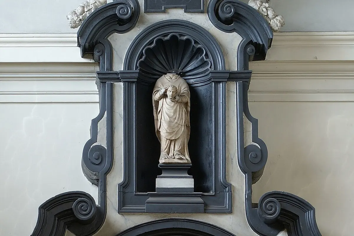 White stone statue of a saint in a niche, set in a black marble Baroque altar frame with a shell canopy and scrolls