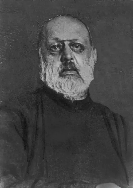 Black-and-white photograph of an older man with a white beard and heavy eyes, wearing a dark collarless habit