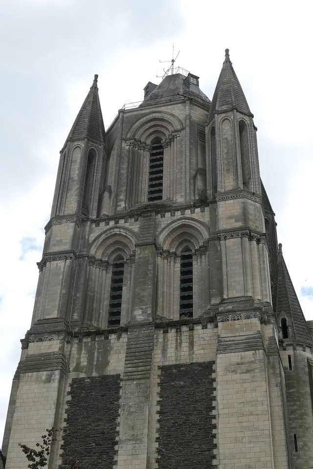 Tall square Romanesque stone bell tower with arched windows and a pointed roof, rising above city buildings under a blue sky