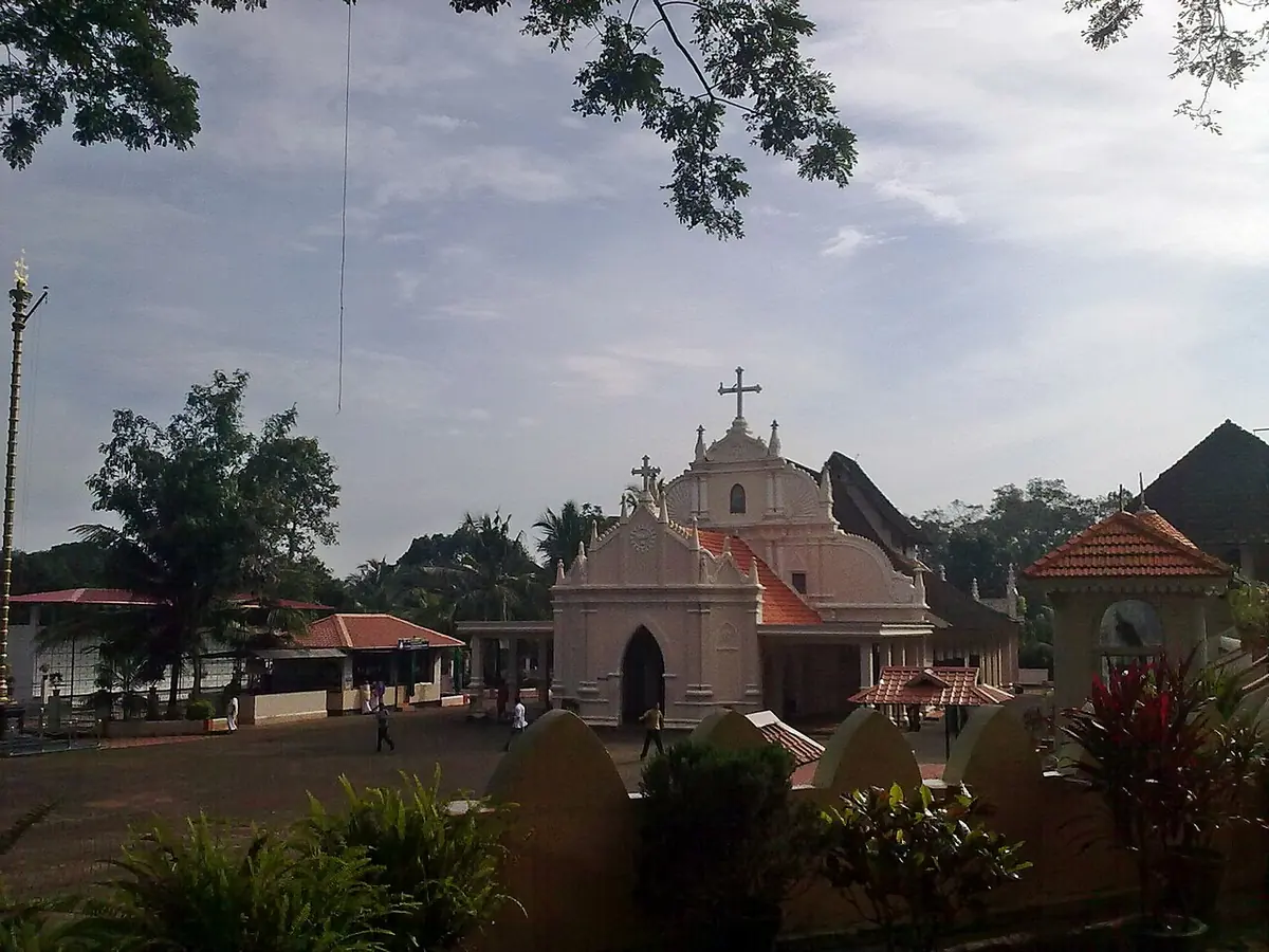 A white and pink church with a cross on its gable, set among trees and lawns in the Kerala village of Kudamaloor