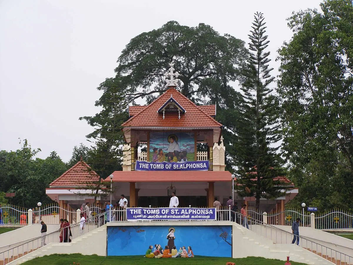 A tiled-roof chapel among tall trees on a rise, reached by a wide stairway with a terraced garden in front