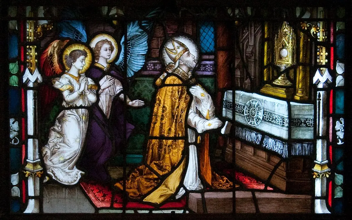 Stained-glass panel of a bishop in gold vestments kneeling before a monstrance on an altar while two angels kneel behind him