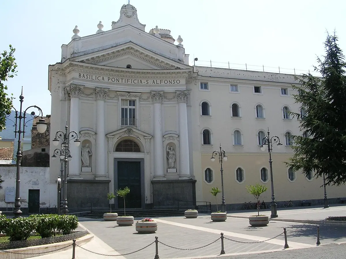 The white neoclassical facade of the Basilica of Sant'Alfonso in Pagani, with a pediment and two statues in niches, beside a long convent building