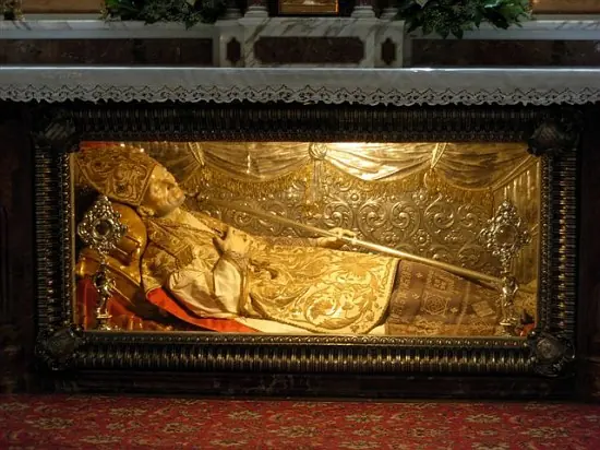 A gilded glass urn beneath an altar holding a reclining figure of St. Alphonsus in bishop's vestments and miter