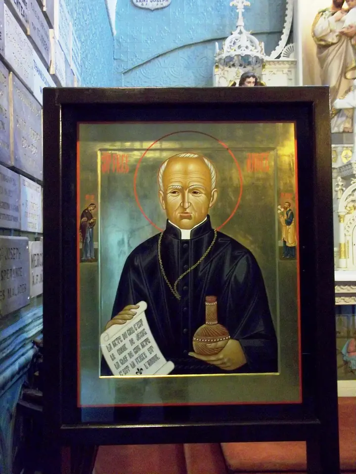 Painted icon of St. André in a black habit with a gold halo, holding a small round bottle of oil and an open scroll