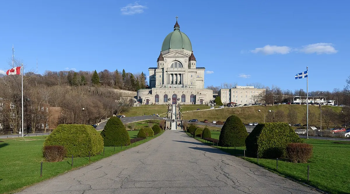 The great domed basilica of Saint Joseph's Oratory on the slope of Mount Royal, seen at the end of a long, tree-lined avenue under a blue sky